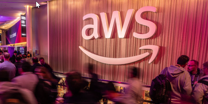 Image of large AWS logo with conference attendees moving in front of it in blurred motion