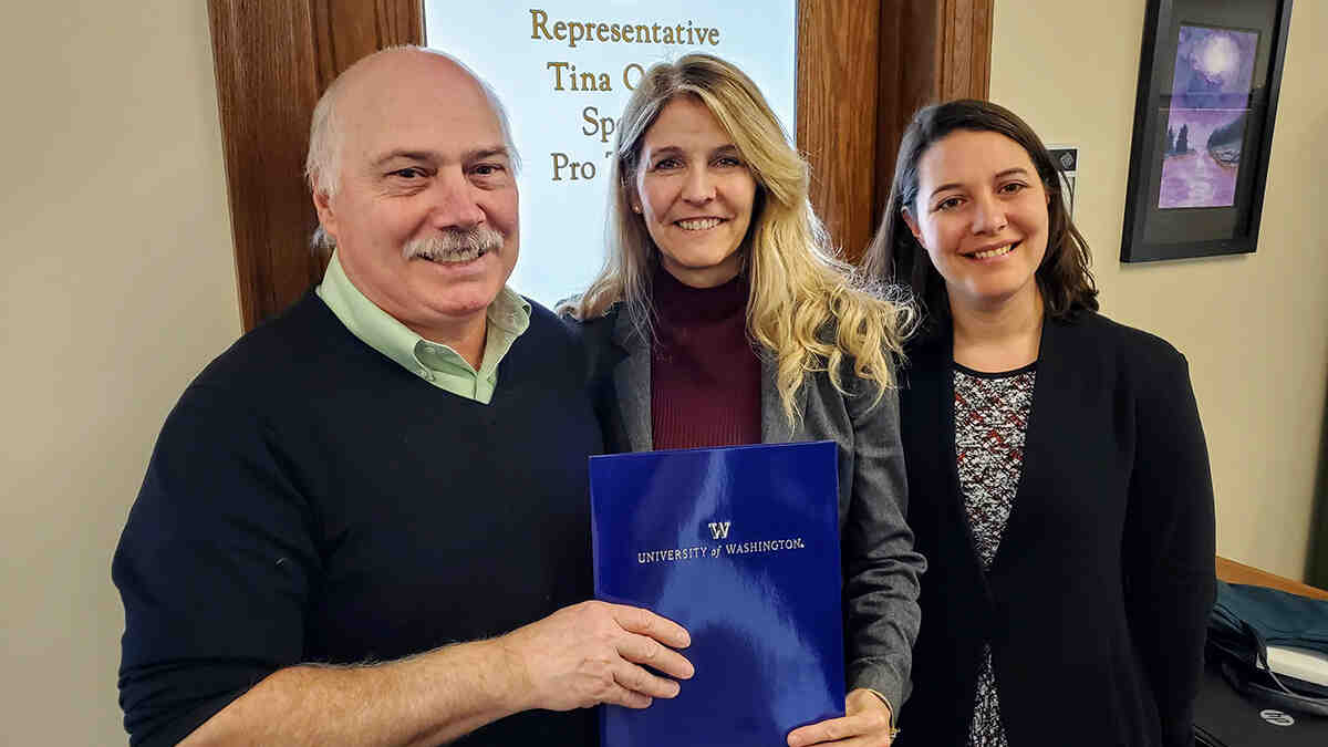 Three department members stand in front of a legislative office holding paperwork.