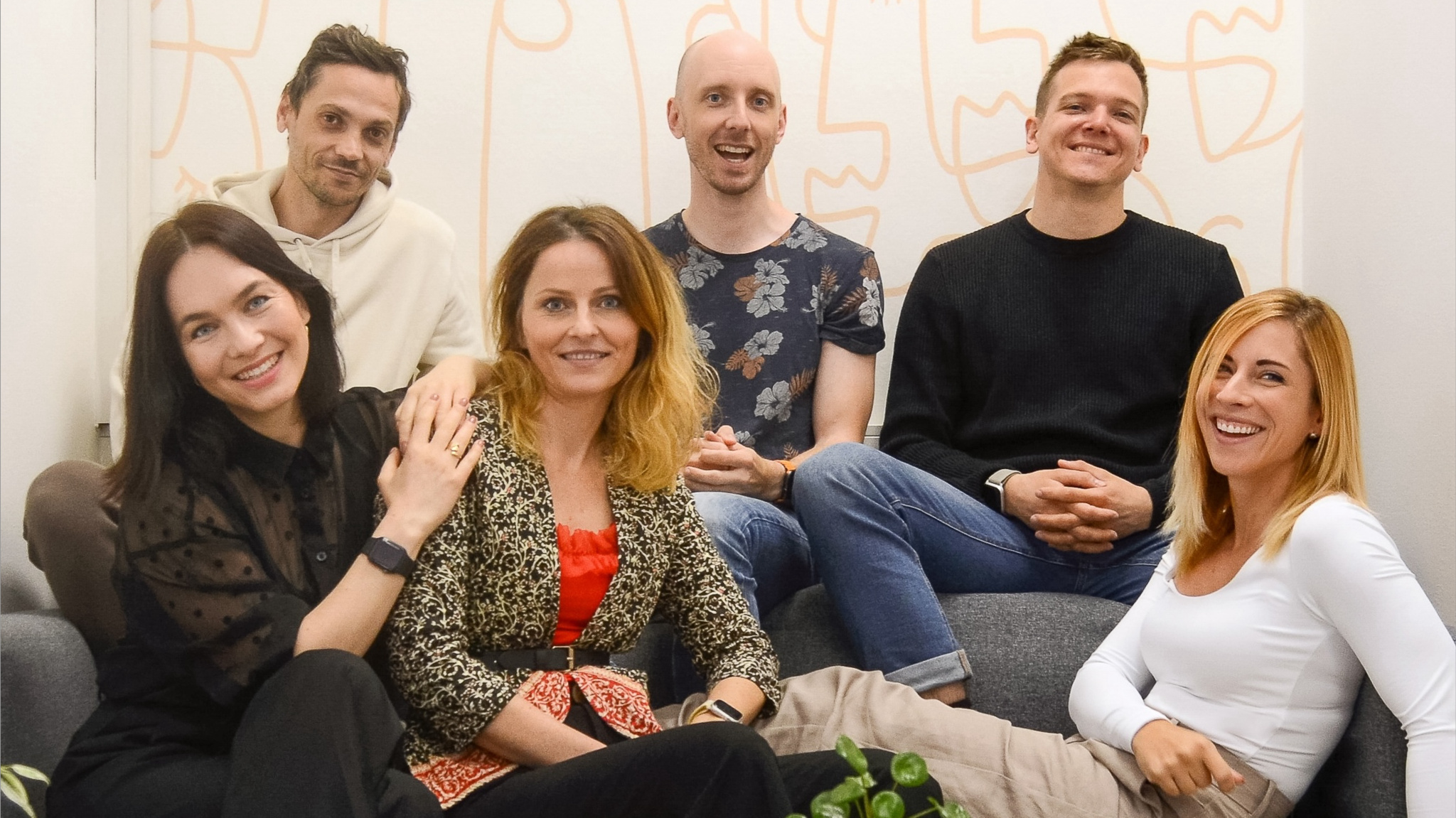 A photo of six members of the Gentler Streak team sitting on a couch in front of a white wall with yellow abstract designs.