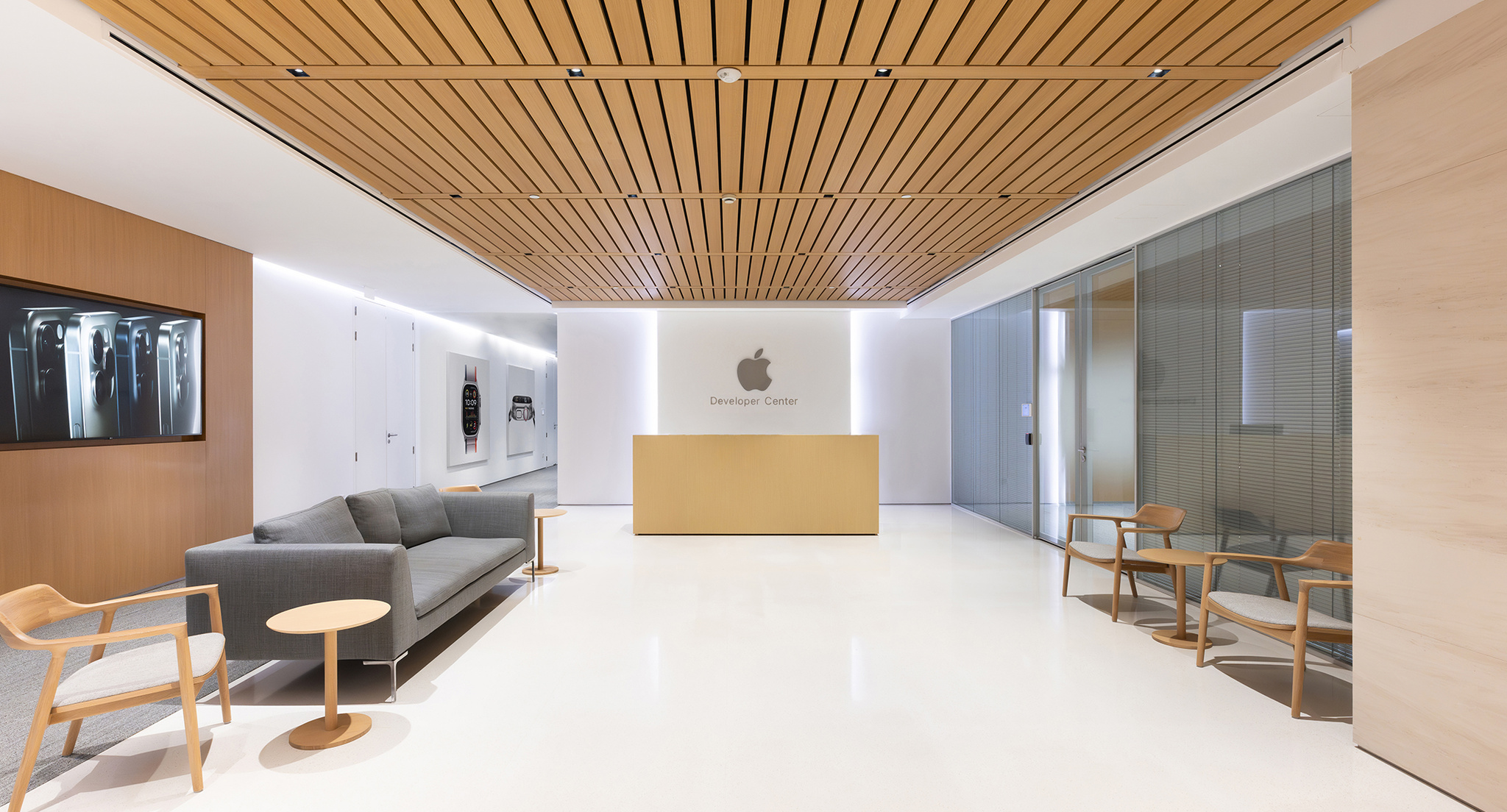 The interior of an Apple Developer Center, an open and brightly lit room with a gray couch, several wooden chairs, and a reception desk that sits underneath a large Apple logo.