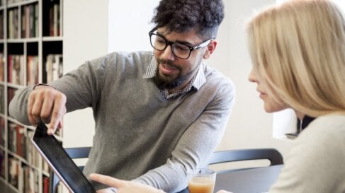 Two college students sit in the library and work on a tablet