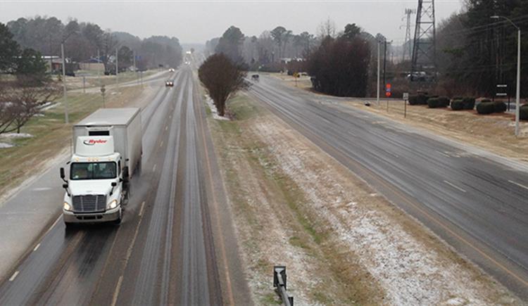 A large semi truck traffic travels along an icy 4-lane highway.