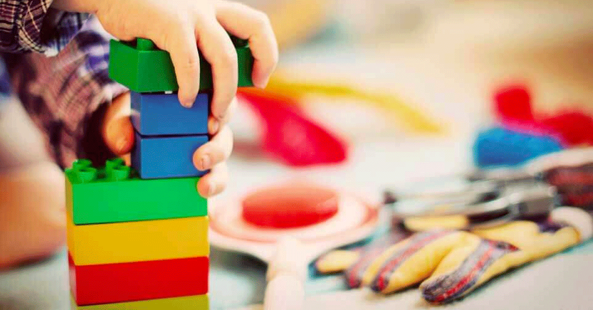 Child stacking Legos while playing on the floor.