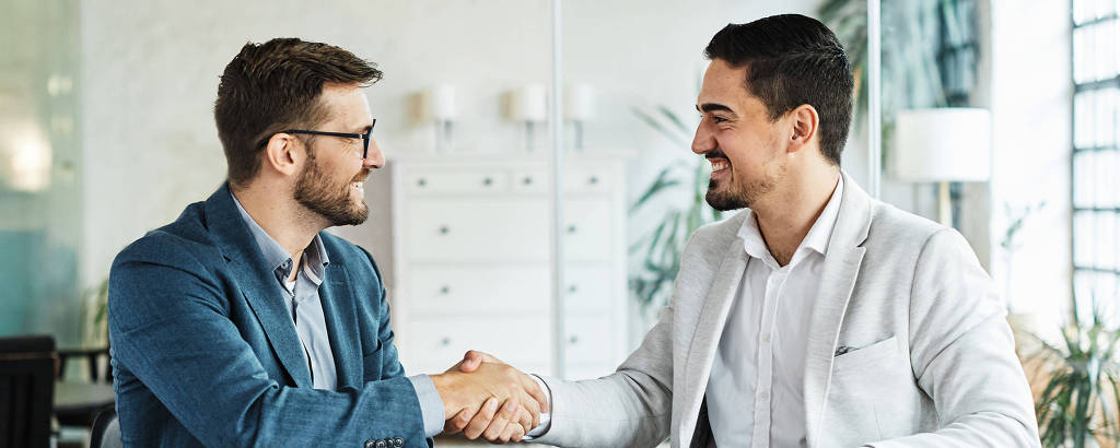 Two happy young businessman shaking hands after signing a contract in the office