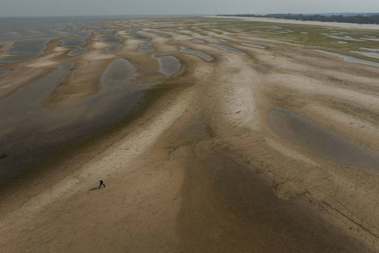 Homem caminha em bancos de areia com pequenas porções de água 