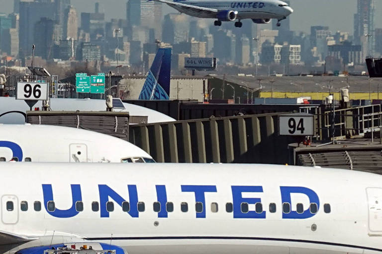 Imagem mostra um avião se aproximando da pista de pouso, enquanto outros aviões estão estacionados