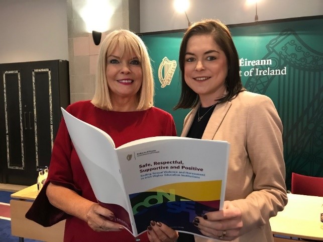 Two women hold a book titled 