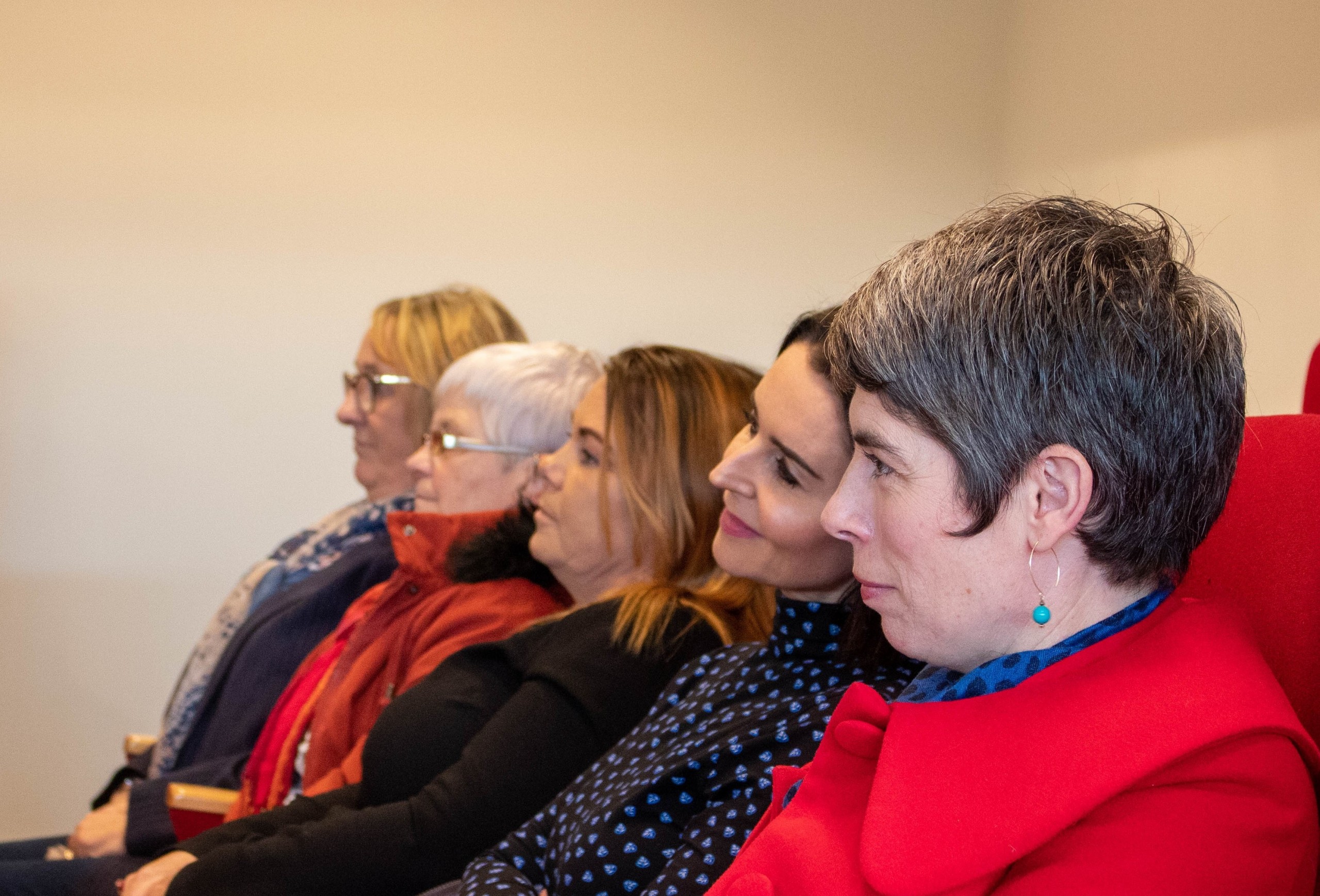 5 women sitting next to each other looking straight ahead to the left of the camera