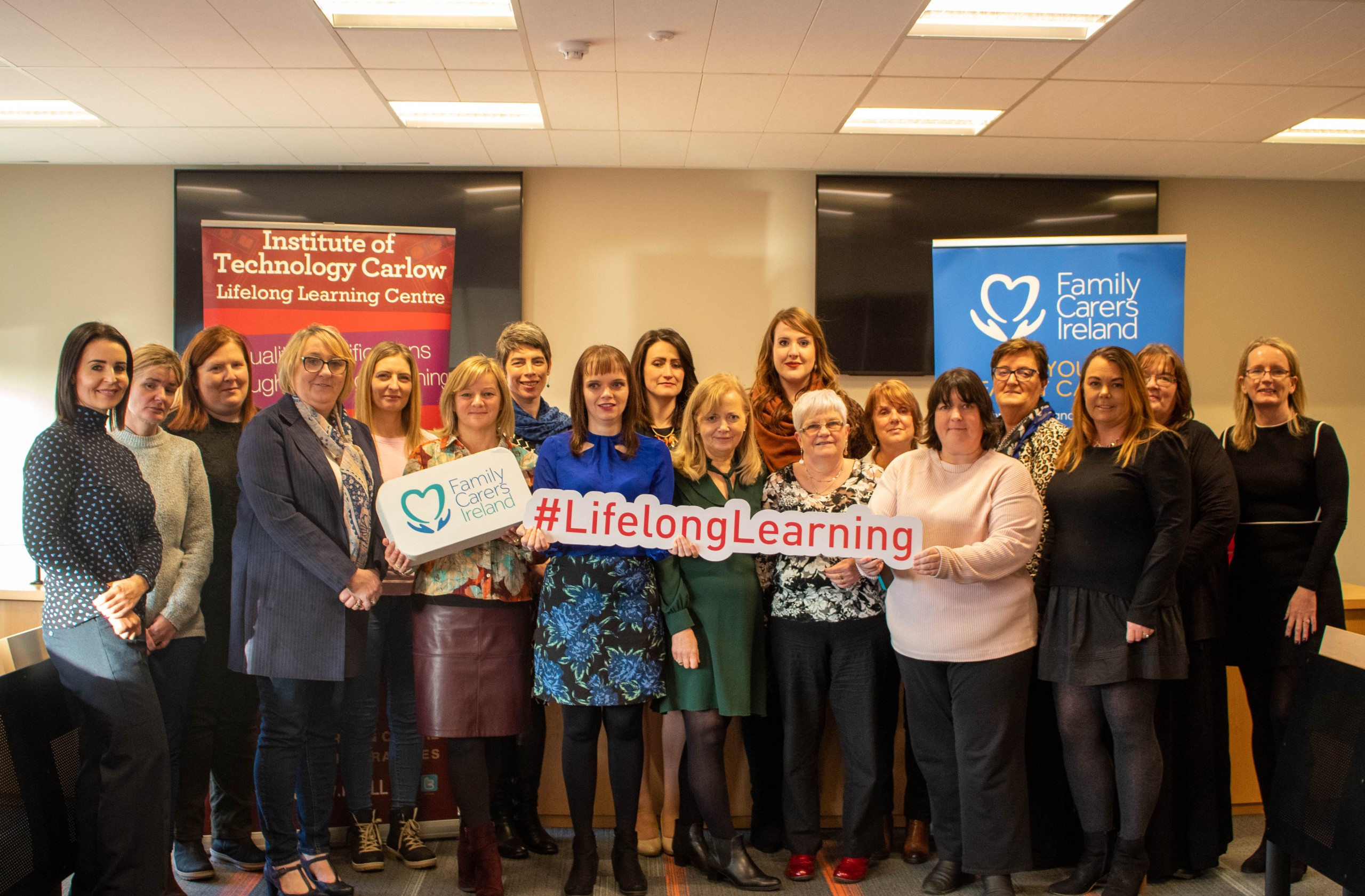 A group photo of a group of people in front of vertical banners, holding a sign saying 