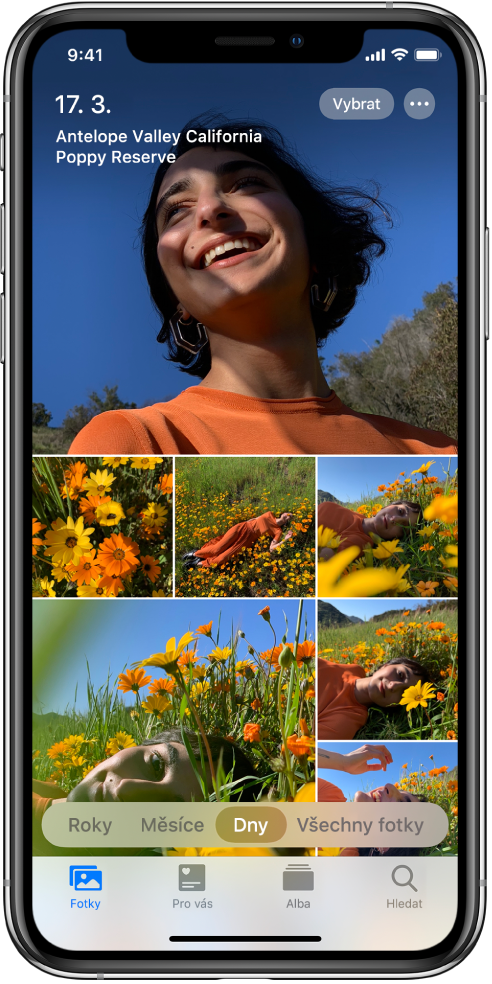 Knihovna fotek v zobrazení Dny. Obrazovka je zaplněna výběrem miniatur fotografií. Vlevo nahoře na obrazovce je vždy uvedeno datum a místo pořízení fotky. Vpravo nahoře jsou vidět tlačítka Vybrat a Další volby; po klepnutí na Vybrat pro sdílet fotky a po klepnutí na Další volby lze zobrazit podrobnosti o fotkách. Pod miniaturami se nacházejí volby pro zobrazení knihovny fotek s uspořádáním Roky, Měsíce, Dny nebo Všechny fotky. Podél dolního okraje jsou vidět panely Fotografie, Pro vás, Alba a Hledat