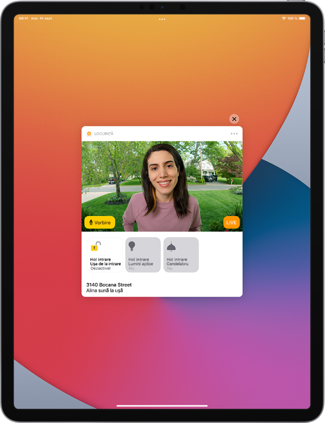 O notificare din aplicația Locuință este afișată pe ecranul iPad-ului. Aceasta prezintă poza unei persoane care este la ușa din față și butonul Vorbire în stânga. Dedesubt se află butoanele accesoriilor pentru ușa din față și luminile de la intrare. Adresa locuinței se află în partea de jos, alături de cuvintele “Alina sună la ușă”. Butonul Închideți se află în partea dreaptă sus a notificării.