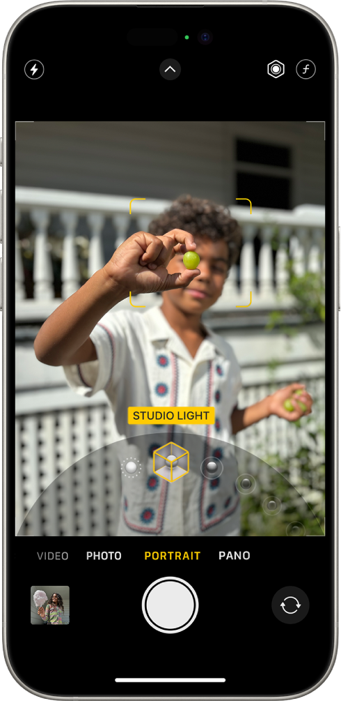 La pantalla de la app Cámara el modo Retrato; en el visor, el objeto se muestra nítido y el fondo difuminado. El dial para seleccionar la iluminación de retrato está abierto debajo del visor, y el efecto Luz de estudio fotográfico está seleccionado. En la parte superior izquierda de la pantalla se encuentra el botón Flash; en la superior central, el botón Controles de cámara; y, en la superior derecha, los botones para ajustar la intensidad de la iluminación de retrato y el control de profundidad. En la parte inferior de la pantalla, de izquierda a derecha, se encuentran los botones Visor de fotos y videos, Tomar foto y Selector de cámara posterior.
