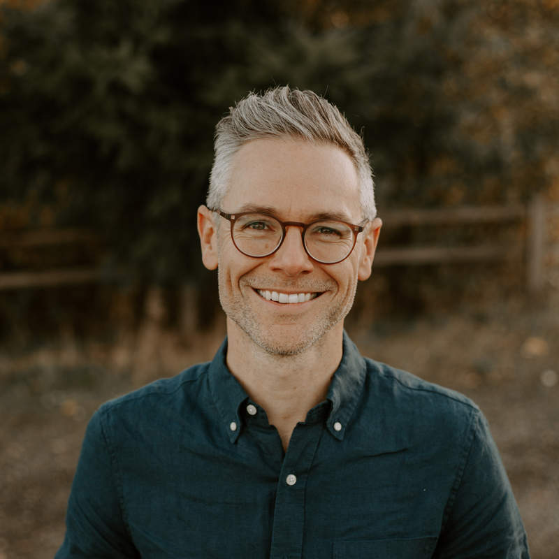 Photograph of Tim Mackie standing in front of a line of trees in Fall