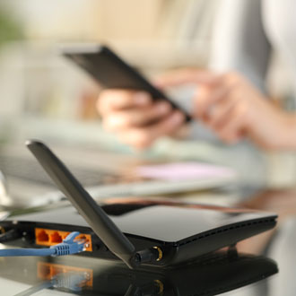 Close-up of a Wi-Fi router on a glass table with a Galaxy tablet being used in the background by a person, illustrating a scenario of troubleshooting Wi-Fi connection issues.