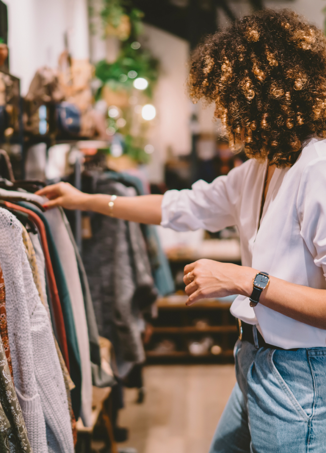 Person with curly hair browses clothing rack in a store.