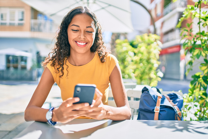 Pretty young women in an orange tee shirt looking at her phone and smiling. 