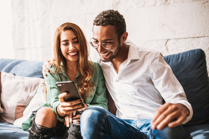 Cute young couple sitting on the sofa looking at a smartphone. 