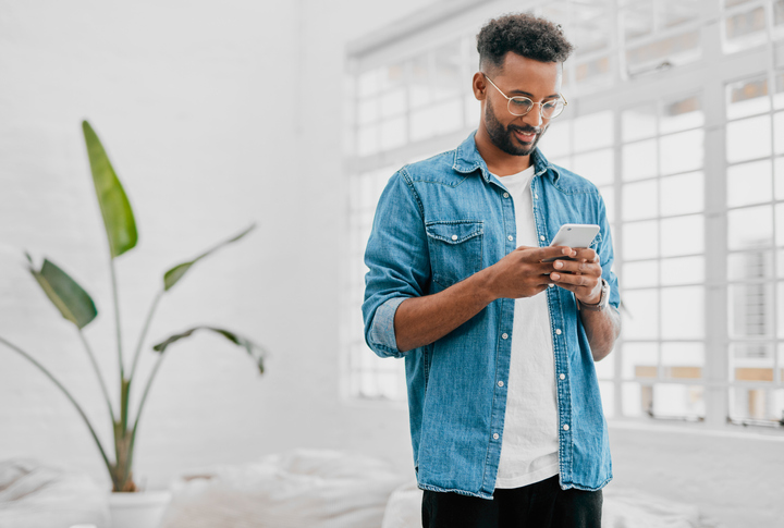 Young man in glasses and a blue denim shirt sending a text. 