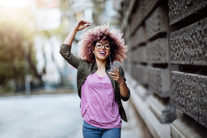 High energy young woman striding down the street listening to music on her cell phone.