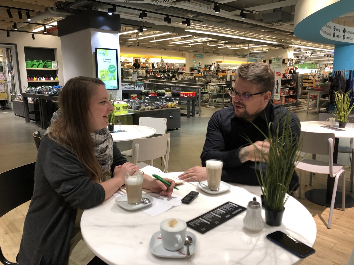 Links Frau, rechts Mann - sitzen an einem Tisch im Geschäft und unterhalten...