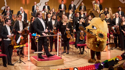 Die Maus steht auf der Bühne vor dem WDR-Sinfonieorchester.