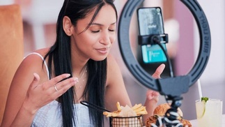 Influencerin vor Handykamera, vor ihr ein Burger und Pommes