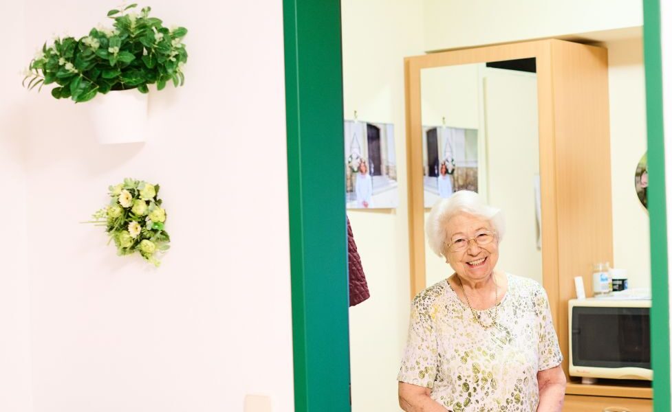 Eine Seniorin steht im Türstock einer Wohnung.