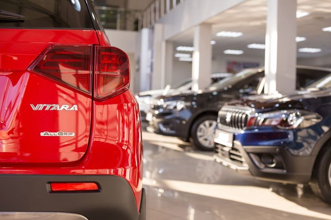 Une vitara rouge est garée dans un showroom à côté d'autres voitures.