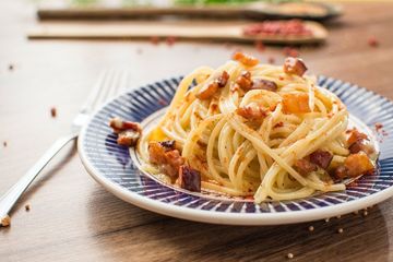 Ein Teller Spaghetti mit Speck auf einem Holztisch mit einer Gabel.