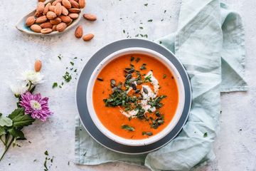 Eine Schüssel Tomatensuppe mit Nüssen und Blumen auf einem Tisch.