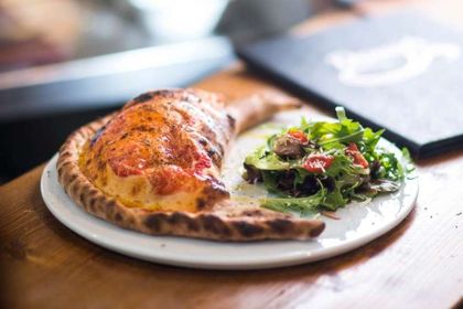 Ein weisser Teller mit einer Calzone-Pizza und einem Salat auf einem Holztisch.