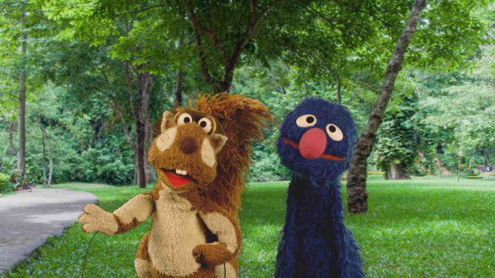 Grover stands next to a squirrel in a park.