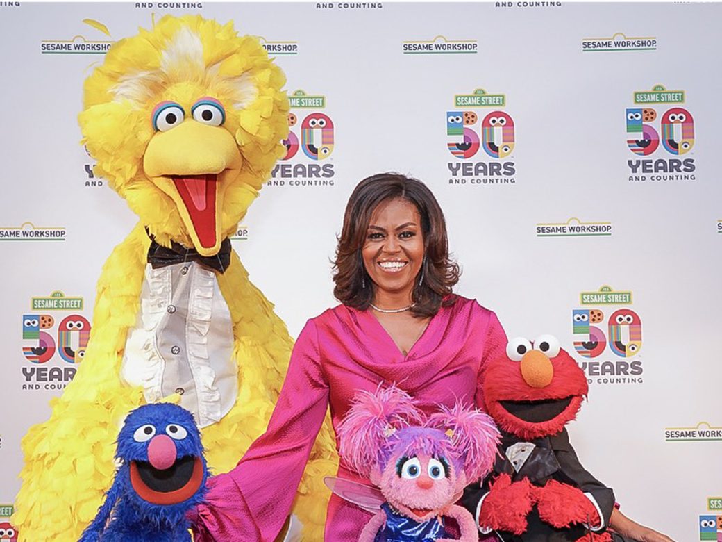 Michelle Obama poses next to Big Bird, Grover, Abby, and Elmo. Everyone is dressed in formal wear.