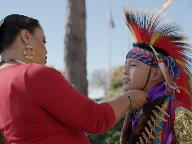 An adult adjusts a traditional Native American headpiece of a child.