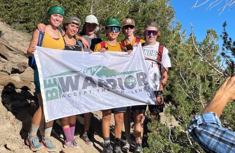 Group of friends holding a Be A Warrior fundraiser flag