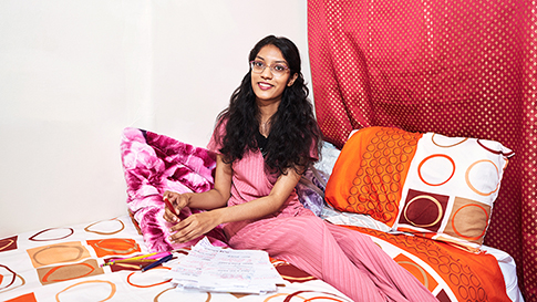 Sabiha sitting on her bed with papers of lecture notes