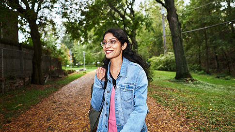 Sabiha smiling and walking down a leaf covered path