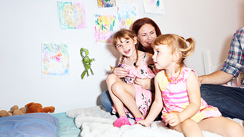 a mother sitting in bed holding her two young daughters while smiling