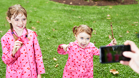 a father using a smartphone to take a picture of his two daughters making a funny face and laughing