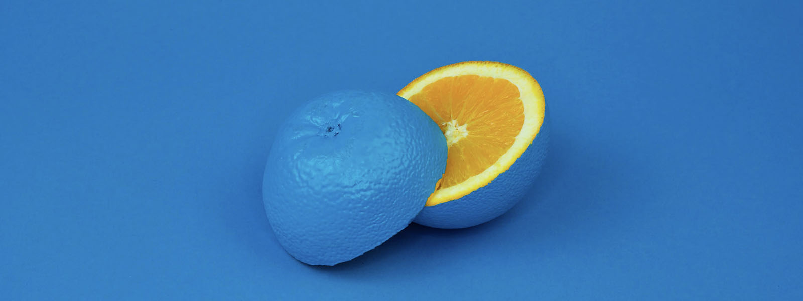 An orange with blue paint covering the peel sliced in half on a blue background