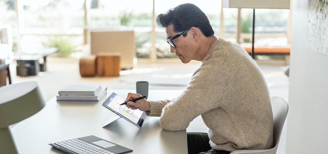 A man sitting in a shared space taking notes on a tablet.