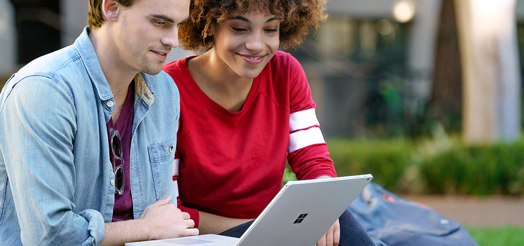 Two people smiling while using a tablet to study.