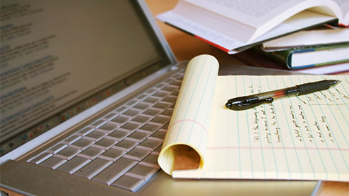 Laptop computer with books, pen and yellow legal pad