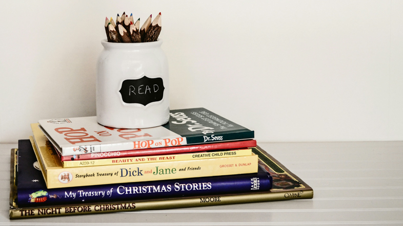 A mug with pencils on top of a stack of books