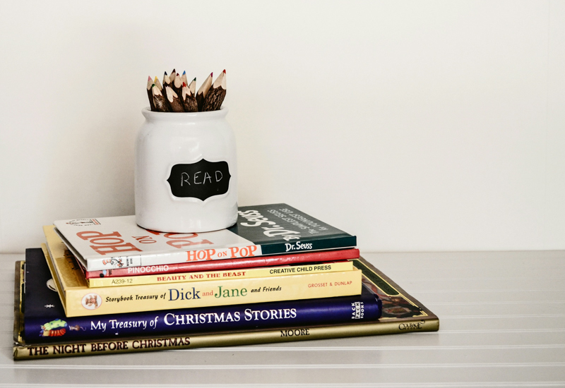 A mug with pencils on top of a stack of books