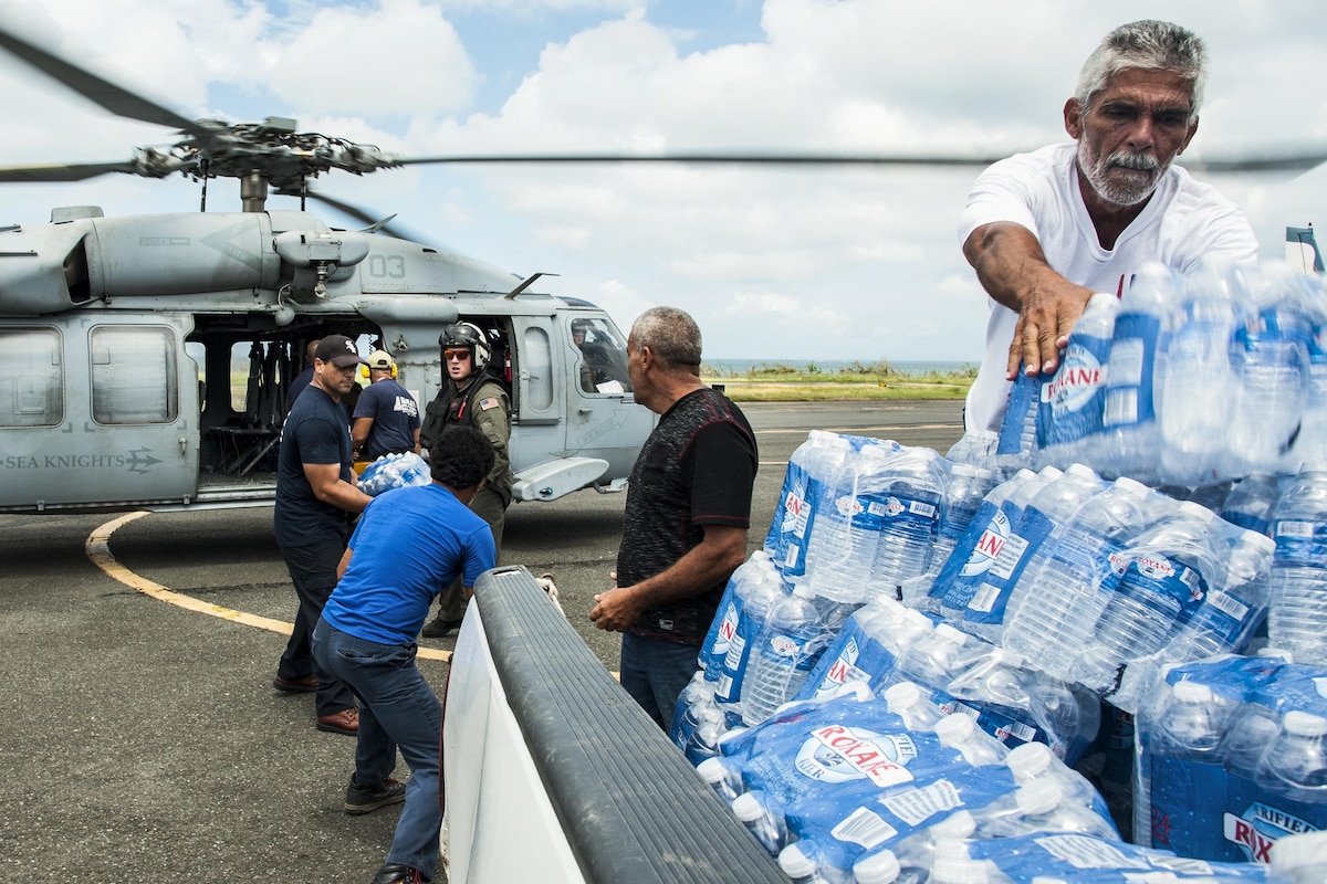 Sailors and others unload relief supplies from a helicopter.