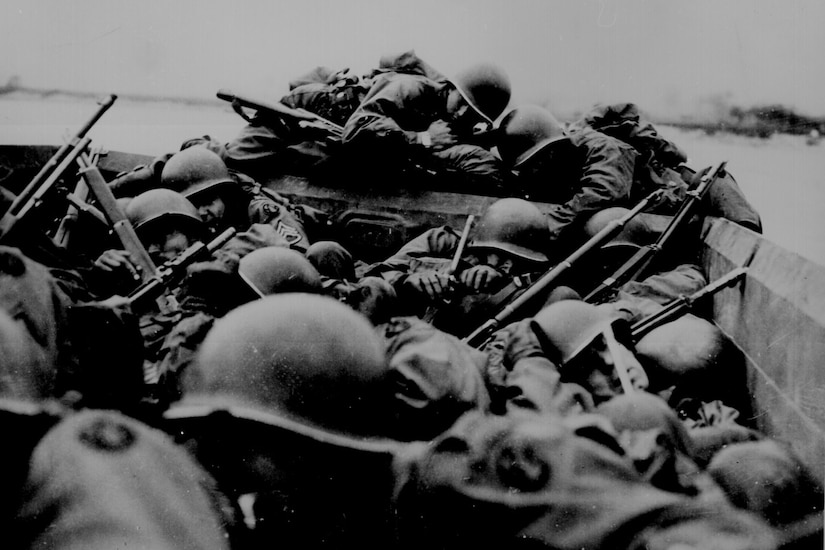 Troops crowd into a boat as it crosses a river.