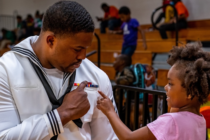 A  young girl points to the insignia on a sailor's uniform.