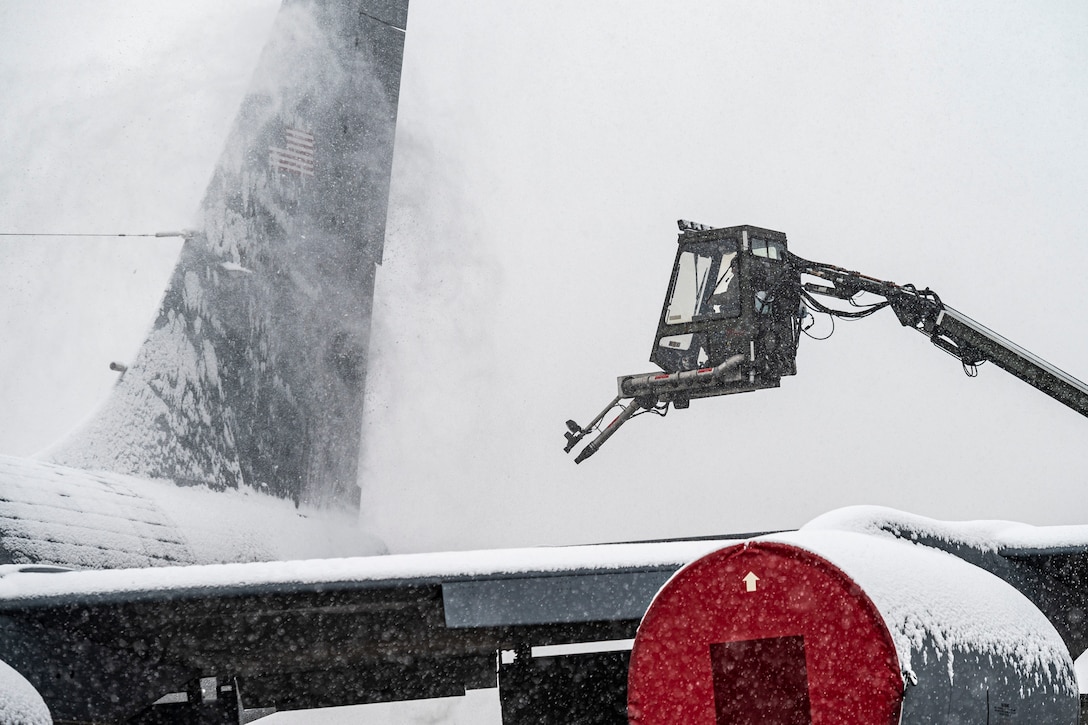 A deicer elevated from a mechanical appendage blows snow off the body of an aircraft.