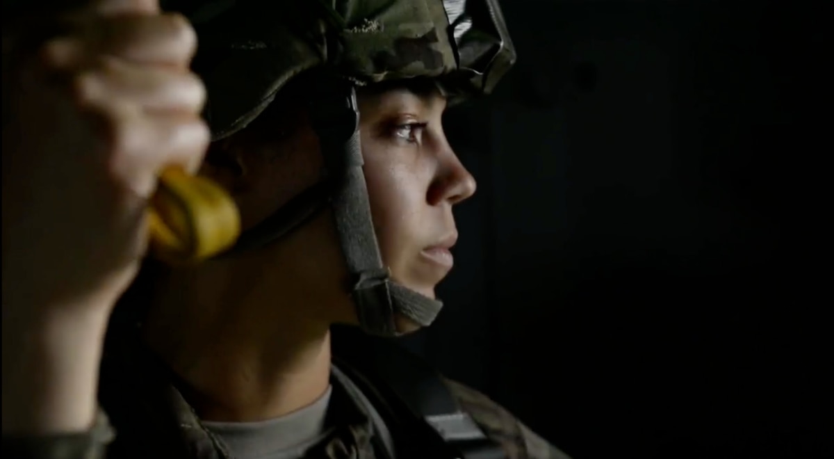 Three military individuals look at a hologram interface.